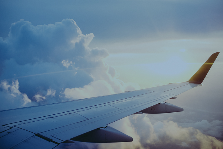 Wing of an airborne plane with clouds and the sky in the background